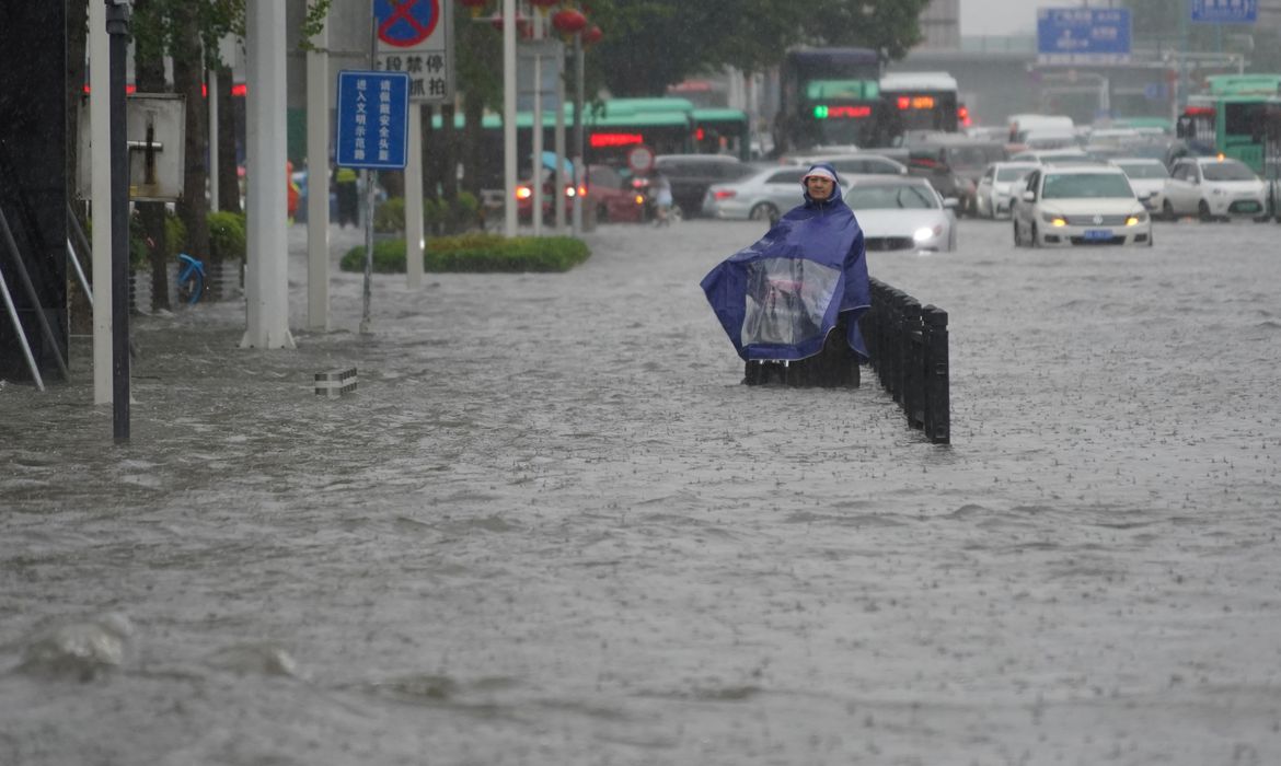 Morador com capa de chuva caminha por rua inundada em Zhengzhou, na província chinesa de Henan.